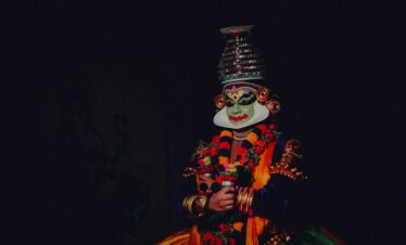 Colorful traditional Kathakali dancer with a distinctive mask on a black background.