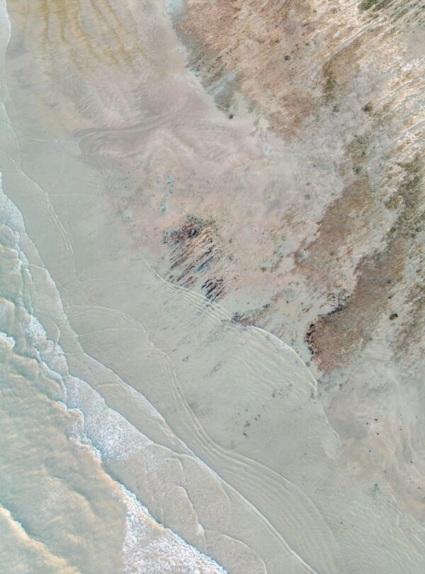 Aerial view capturing the tranquil meeting of ocean waves and sand on a serene beach.